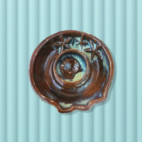 Overhead view of a rich red-brown round ceramic incense burner dish with a relief sculpture of three starfish. The incense burner is sitting on a pale seafoam green background.