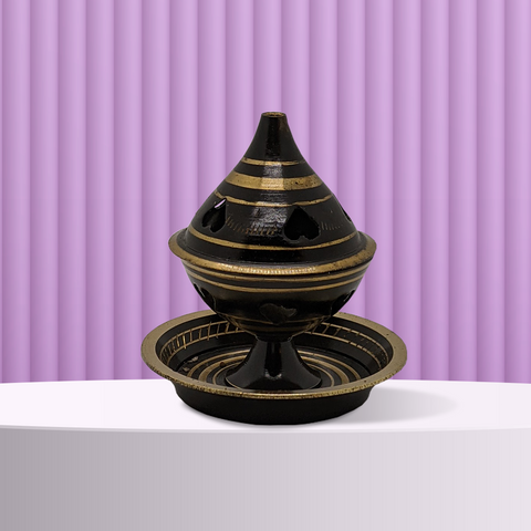 An incense cone burner that resembles an egg cup with a circular base, rounded cup to hold the incense cone, and a lid that comes to a point with a hole on top for the incense smoke to escape. The cone burner is black with decorative horizontal gold stripes and upside down heart shaped holes on the lid, and is sitting in front of a light purple background.