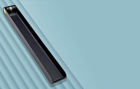 A long black metal incense burner featuring a brass knob at one end that is used to adjust the angle of an incense stick. The burner is sitting on a blue-grey backgound. Designed and fabricated by Toronto CNC machine shop Rocket Surgery Solutions.