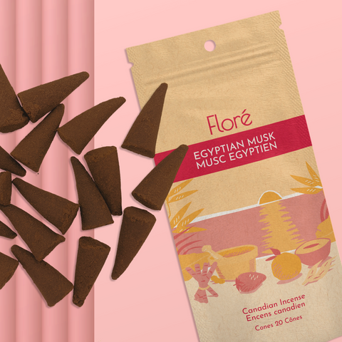 A pale orange package of incense cones that reads Flore Egyptian Musk with an image of red and orange fruits, spices and mortar and pestle on a beach at sunset. The package lies with a bunch of incense cones on a pale red background.