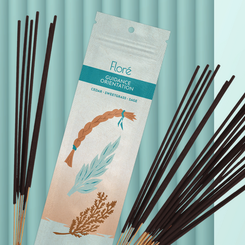 A pale blue-grey package of incense sticks that reads Flore Guidance with an image of a sweetgrass braid, sage leaves and a cedar bough. The package lies with a bundle of incense sticks on a pale aqua background.