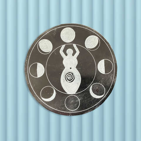 Overhead view of a round flat disk incense burner featuring the moon cycle around the image of a goddess against a grey background. 