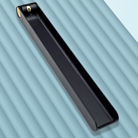 A long black metal incense burner featuring a brass knob at one end that is used to adjust the angle of an incense stick. The burner is sitting on a blue-grey backgound. Designed and fabricated by Toronto CNC machine shop Rocket Surgery Solutions.