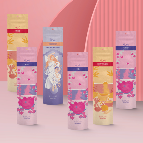 Six different packages of incense sticks standing upright against a pale red background. From left to right the packages include Amber, Rose, Abundance, Lilac, Egyptian Musk and Jasmine.
