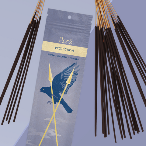 A smoky purple package of incense sticks that reads Flore Protection with an image of a flying crow behind crossed golden spears. The package lies with a bundle of incense sticks on a periwinkle background.