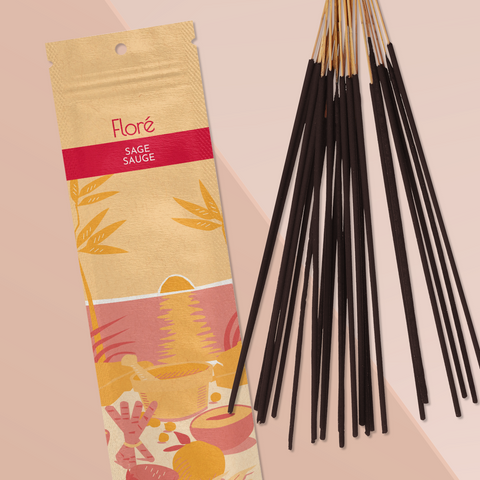 A pale orange package of incense sticks that reads Flore Sage with an image of red and orange fruits, spices and mortar and pestle on a beach at sunset. The package lies with a bundle of incense sticks on a rosy taupe background.