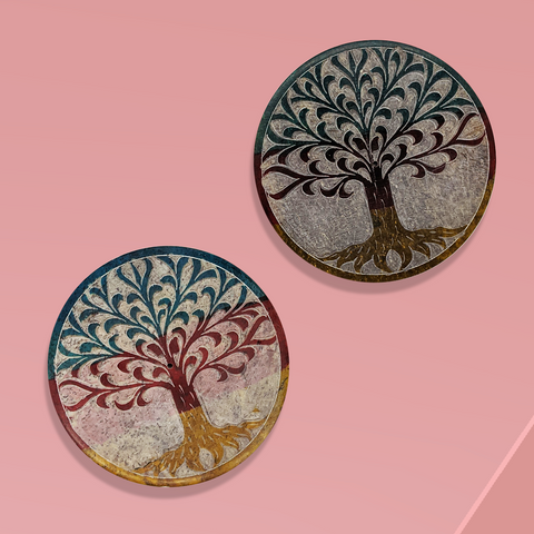 Overhead view of two round flat disk incense burners with a tree of life image on each one against a rosy pink background.