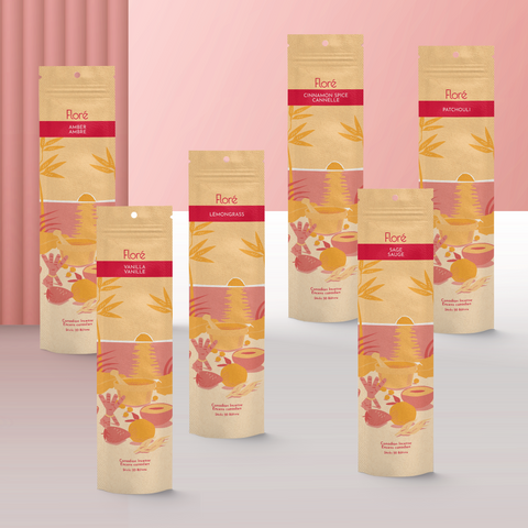 Six different packages of incense sticks standing upright against a pale red background. From left to right the packages include Amber, Vanilla Lemongrass Cinnamon Spice, Sage and Patchouli.