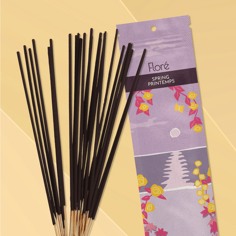 A pale purple package of incense sticks that reads Flore Spring with an image of yellow flowers framing a purple lake with a pink sun in the sky. The package lies with a bundle of incense sticks on a pale golden background.
