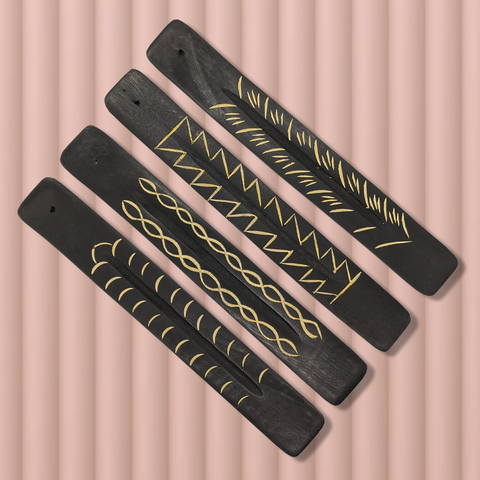 Four long flat black wooden incense burners with unique carvings arranged side by side diagonally against a peach background.